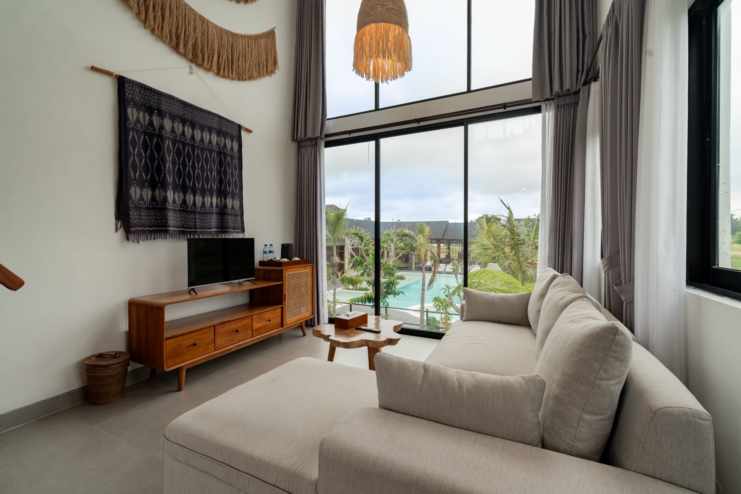 Villa living room with a teak sideboard and a woven ikat textile on the wall, opening onto the resort pool